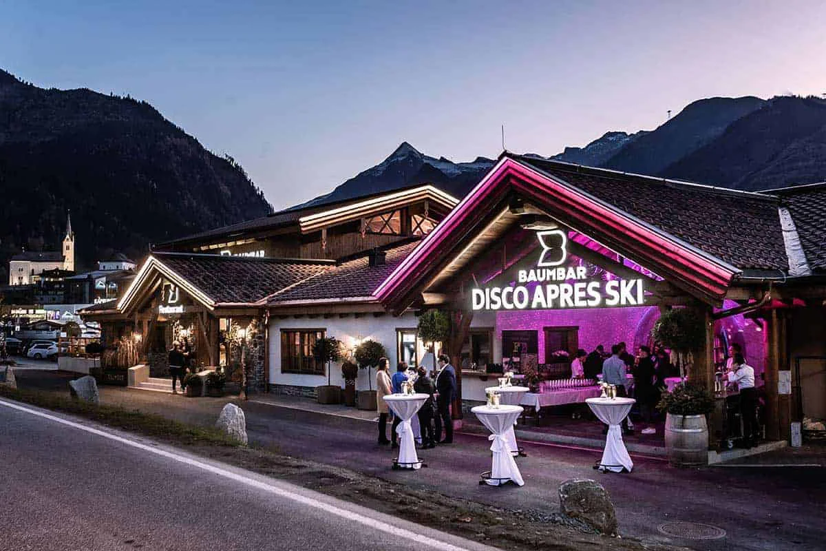 Baumbar Disco Apres Ski mit Lichteffekten vor Bergkulisse bei Dämmerung.